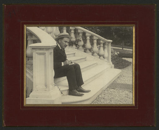 [Portrait photographique de Denys Puech assis sur des marches d'escalier]